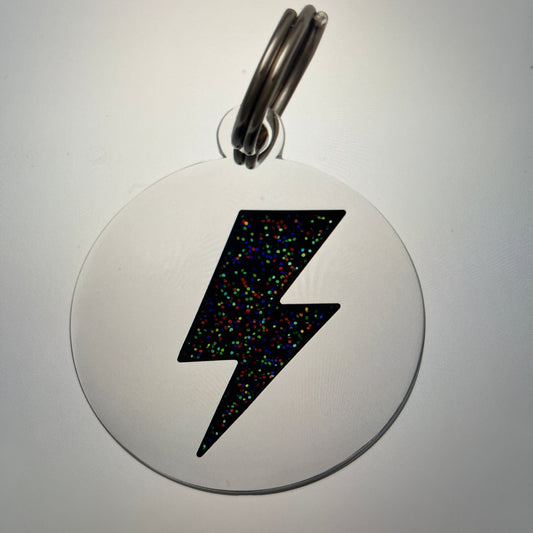 Circular metal badge with a black lightning bolt design on a white background